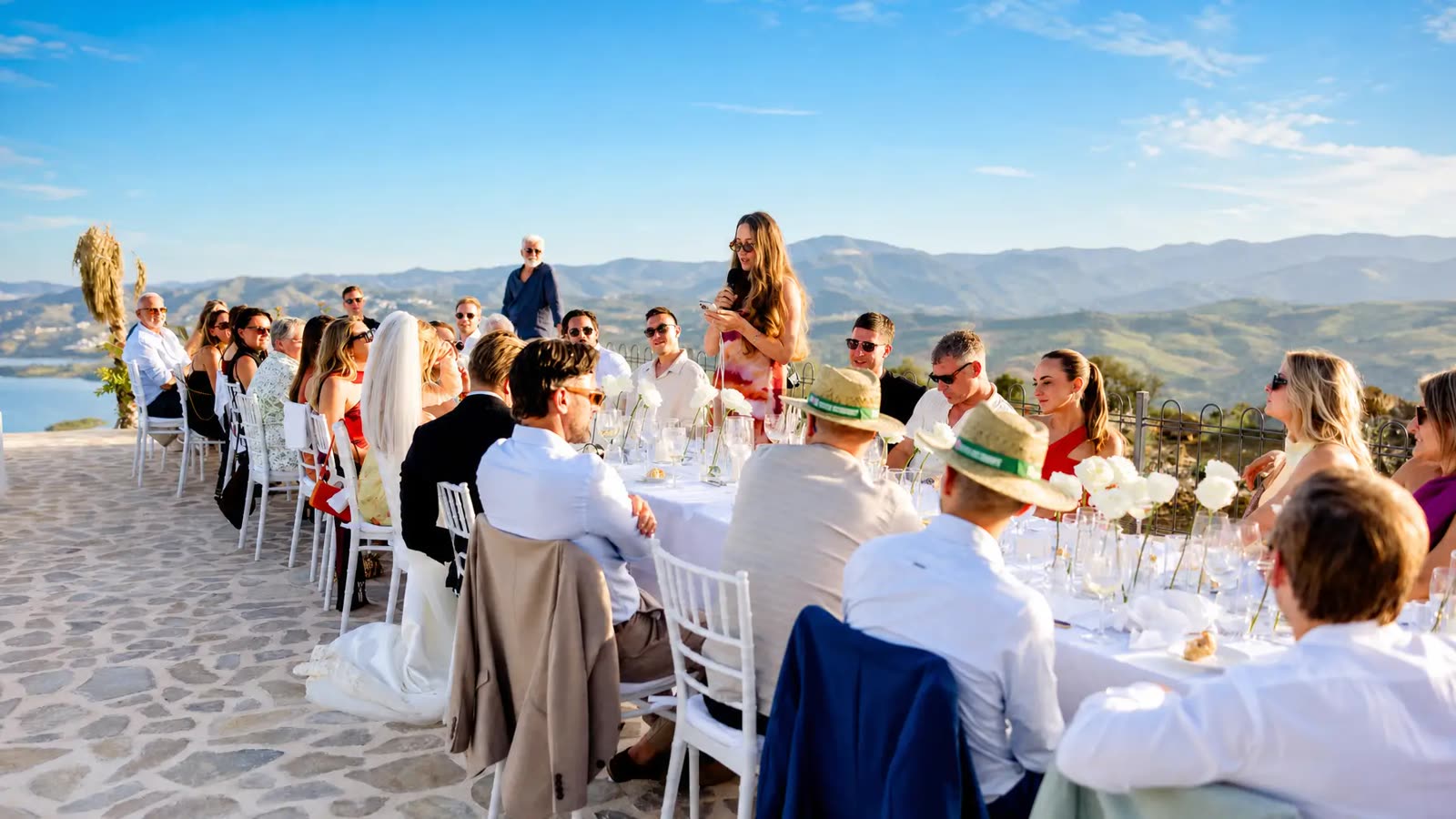 Guest giving a toast at a long wedding table overlooking Lake Viñuela